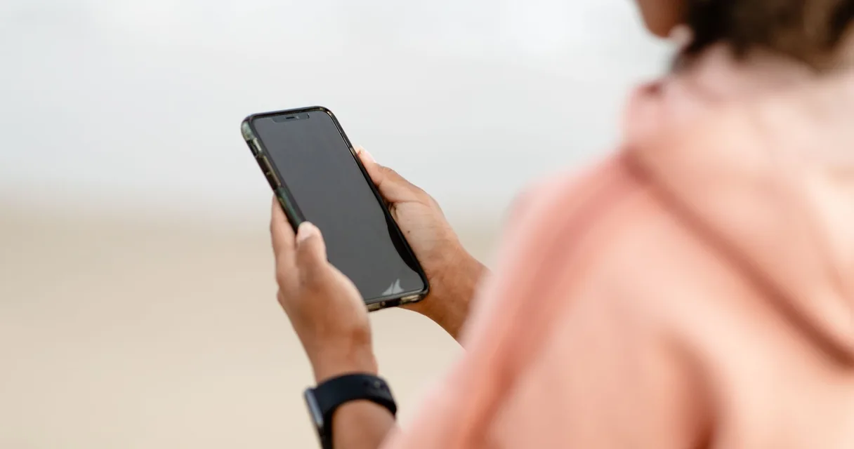 Pessoa vista de costas segurando um celular ao ar livre com a tela apagada